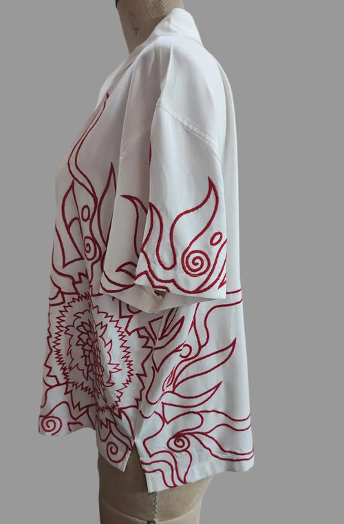 A white short-sleeve button-up shirt with red line-art flame or wave patterns, displayed on a mannequin torso against a plain beige wall.